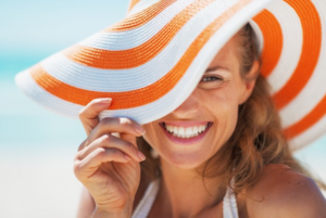 Woman in big floppy beach hat smiling with the sun behind her